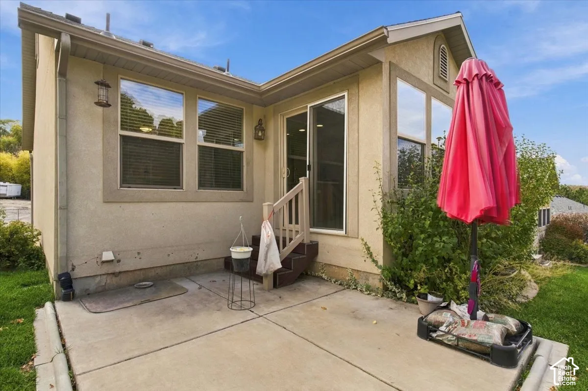 Stucco exterior featuring a concrete patio, sliding glass door, and exterior wall-mounted lighting