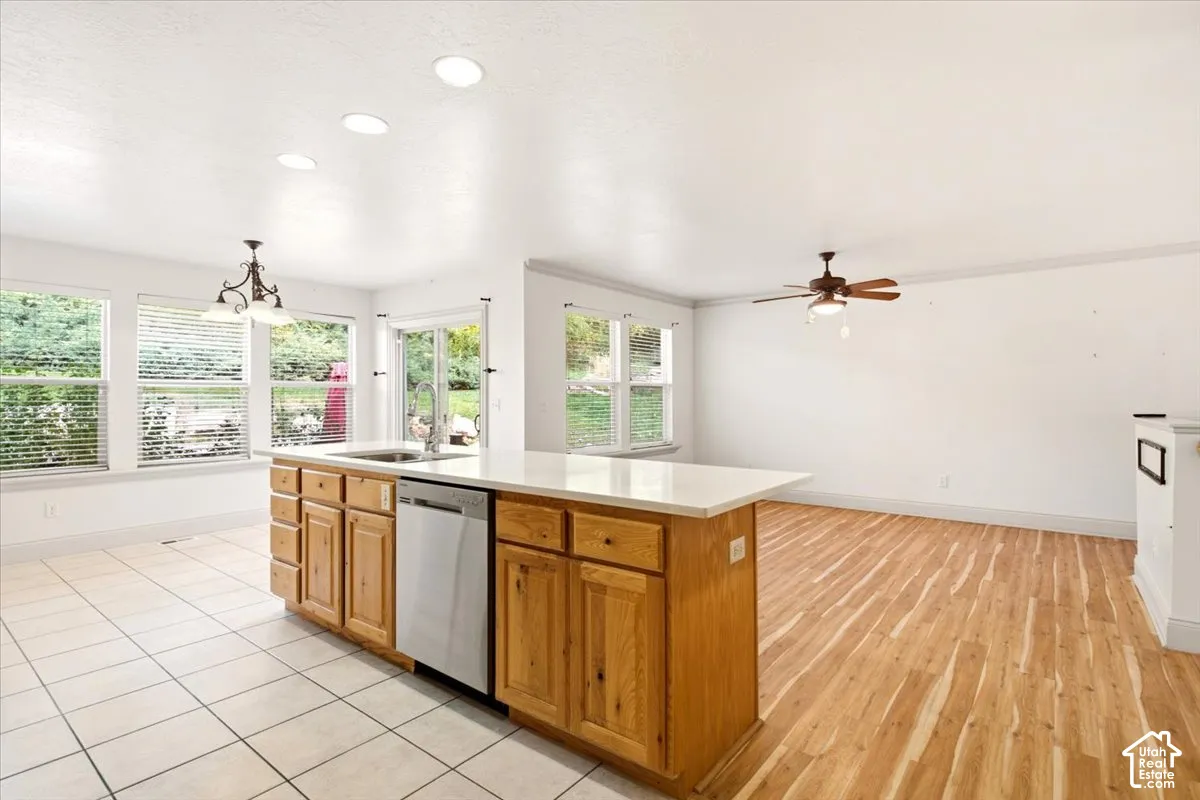 Kitchen island featuring wood cabinetry, a stainless steel dishwasher, and a light-toned countertop