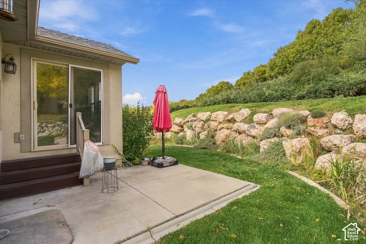 Concrete patio with steps leading to a sliding glass door and tiered stone retaining wall