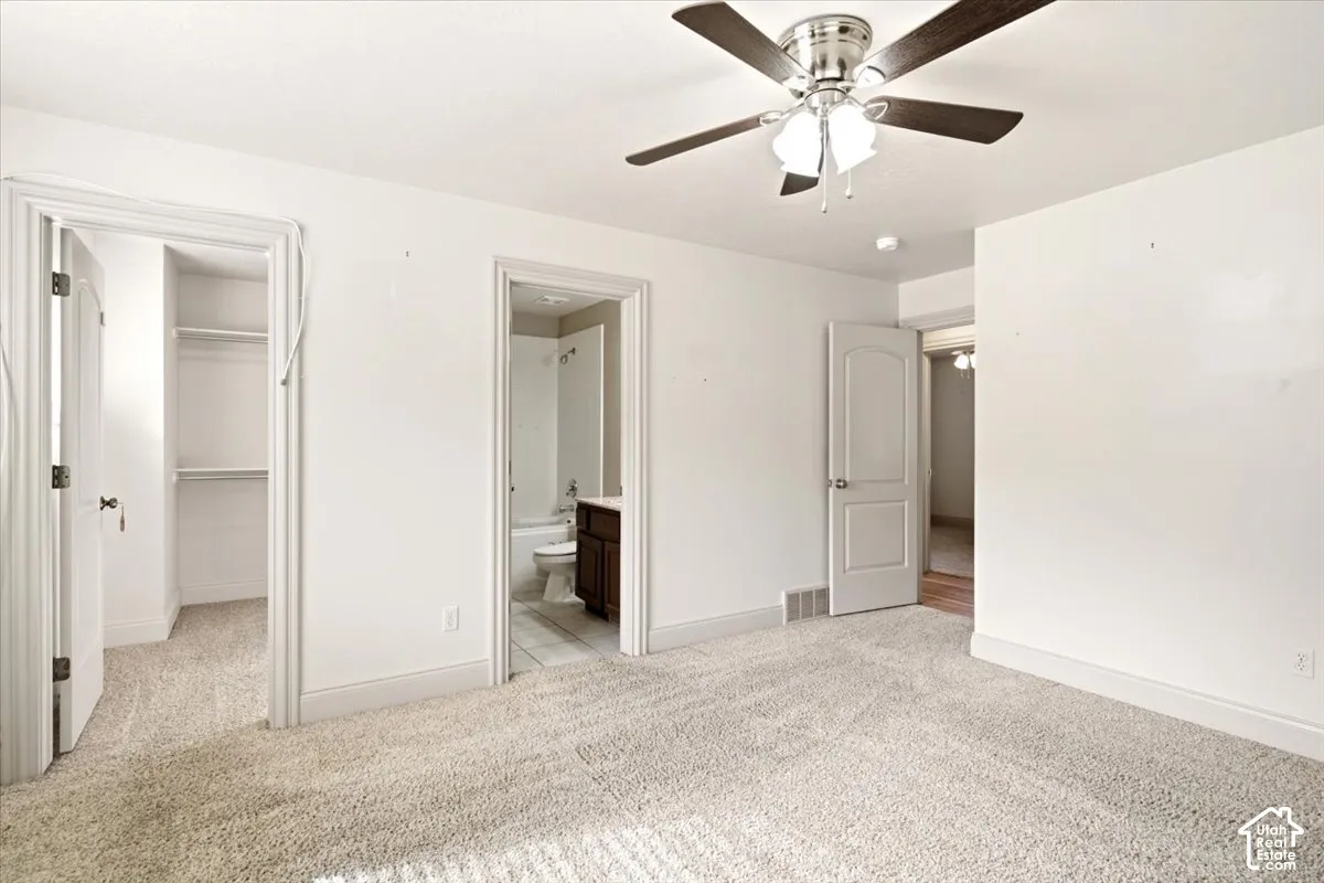 Neutral-toned wall-to-wall carpeting, ceiling fan with integrated lighting, multi-panel interior doors, and built-in closet shelving