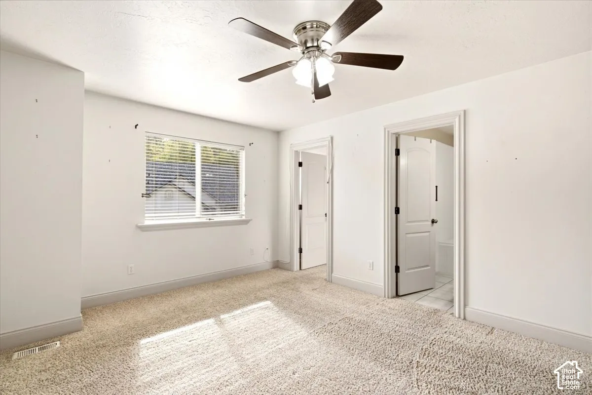 Neutral carpeted room featuring a ceiling fan with integrated lighting, two panel-style interior doors, and a single-hung window with horizontal blinds