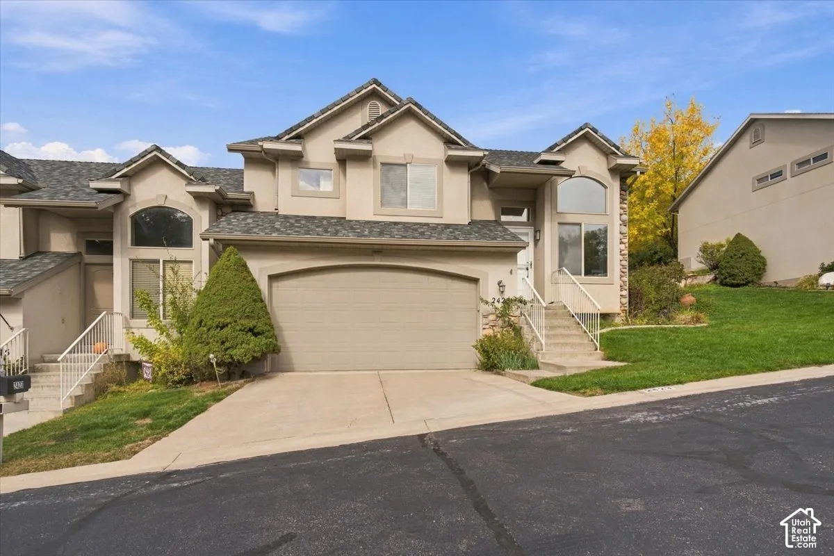 Stucco exterior featuring an arched garage door, gabled rooflines, multiple windows with arched accents, and concrete stairs with metal railings