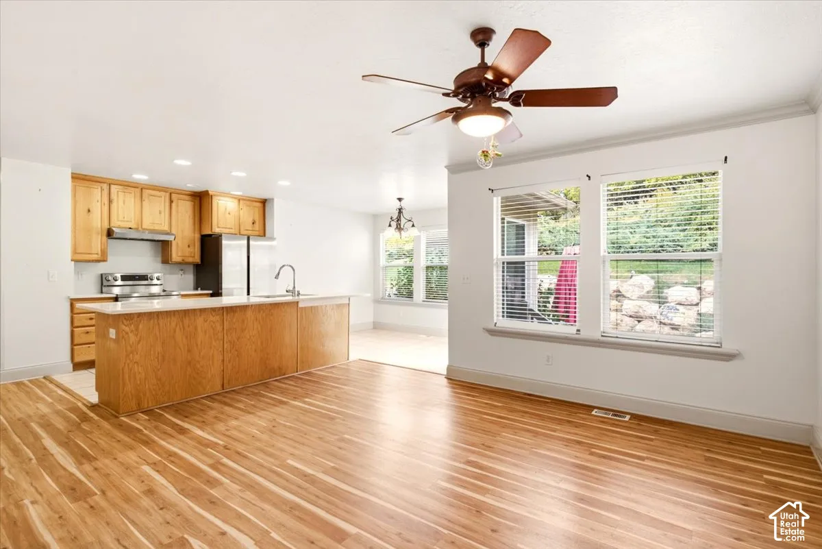 Kitchen featuring wood-finish cabinetry, a central island with countertop seating, wood-finish flooring, recessed lighting, and a ceiling fan