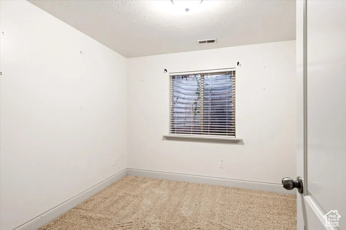 Neutral-toned carpet flooring, window with horizontal blinds, and window well egress