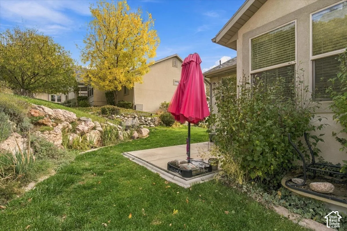 Exterior space featuring a concrete patio, tiered stone landscaping, and a manicured lawn