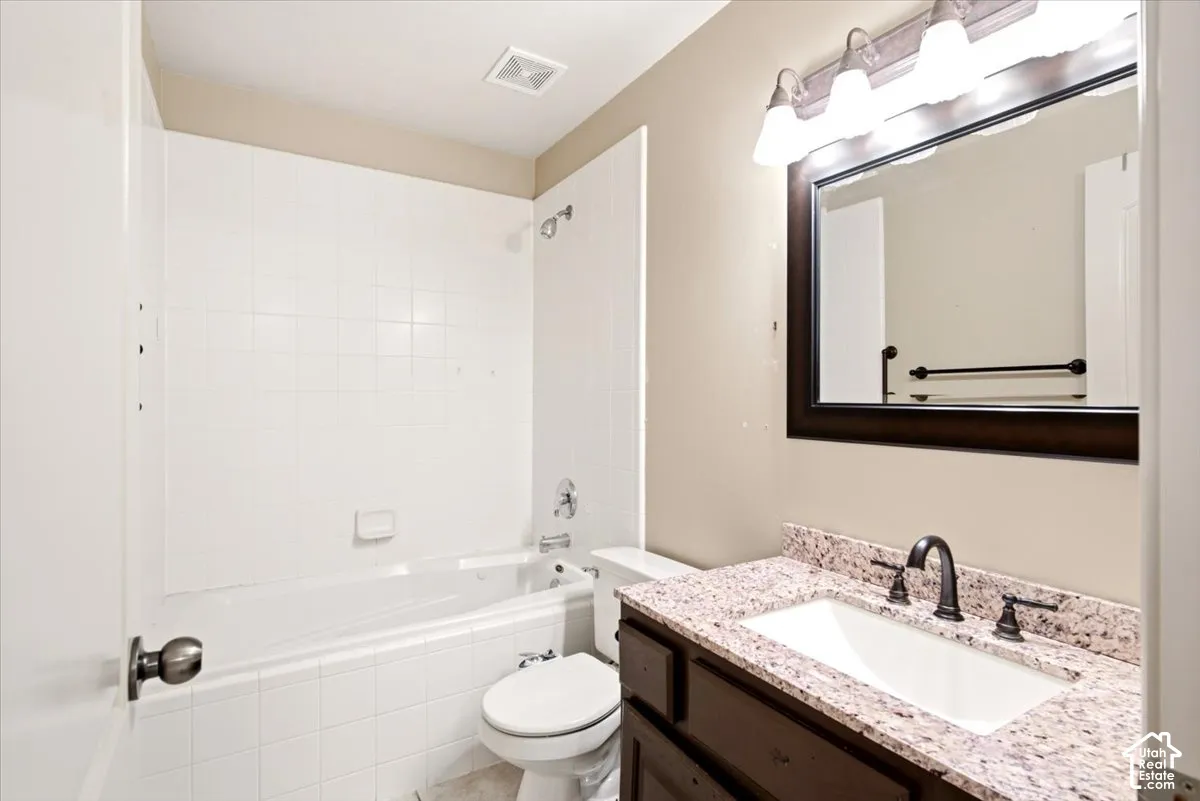 Bathroom featuring a stone-surface vanity with an integrated undermount sink, dark-finish cabinetry, a framed wall mirror, and a tile-surround shower and tub combination