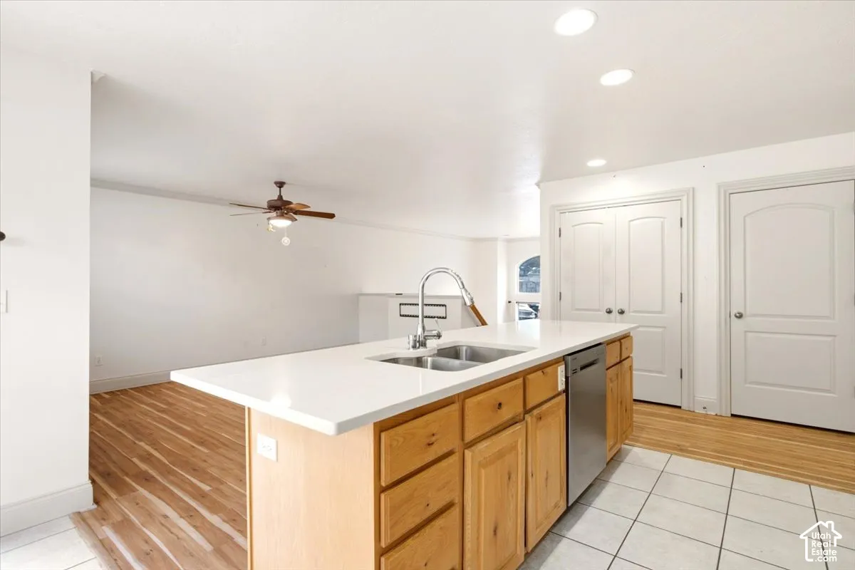 Kitchen island featuring a solid-surface countertop, dual-basin stainless steel sink, wood-finish cabinetry, built-in dishwasher, and recessed lighting