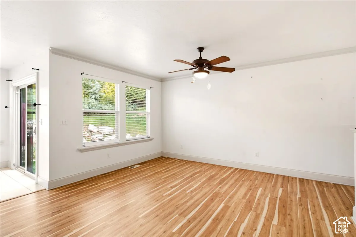 Interior space featuring wood-finish flooring, crown molding, a ceiling fan with integrated lighting, and dual windows