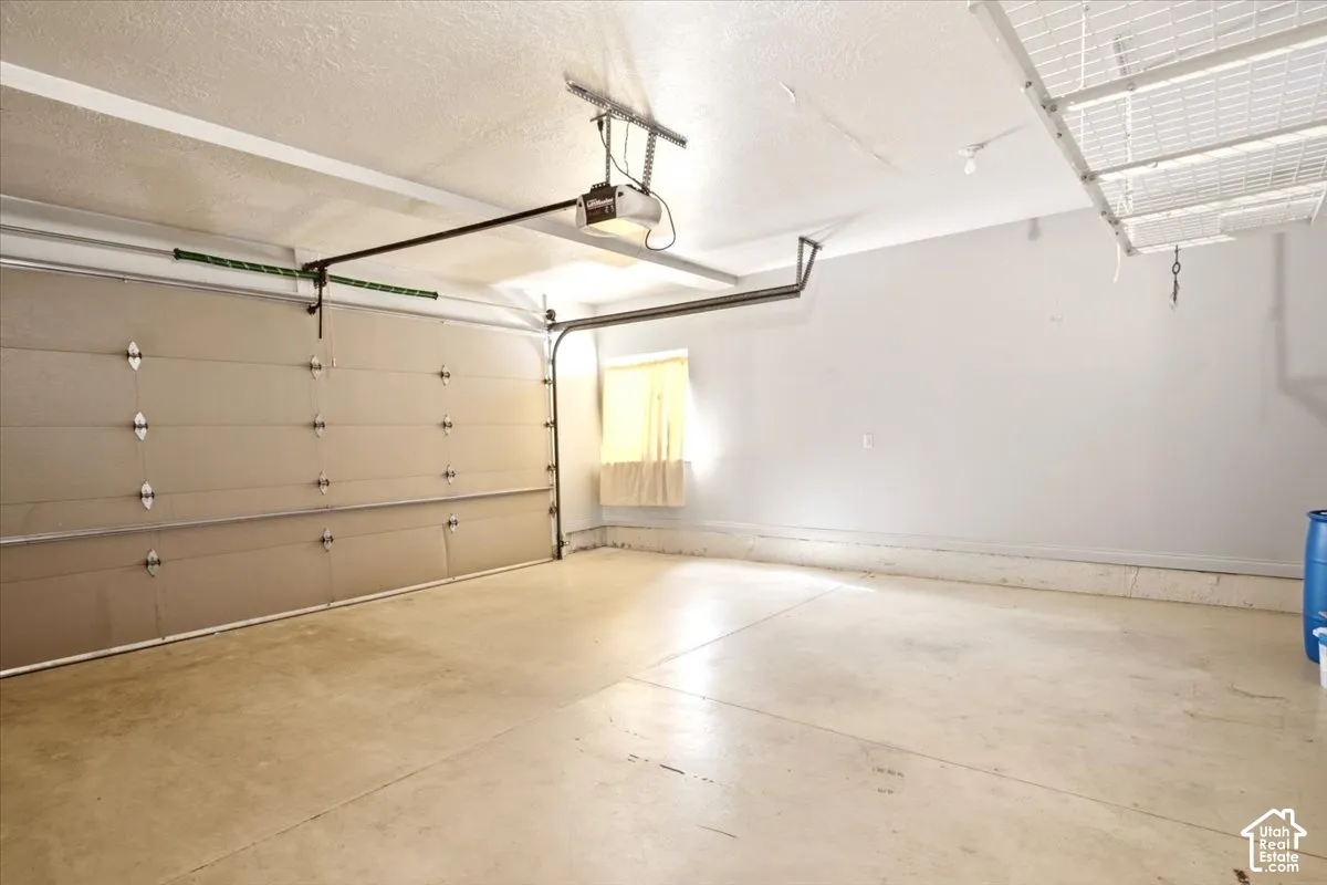 Garage space featuring a paneled sectional door, concrete flooring, overhead storage racking, and a mounted automatic door opener