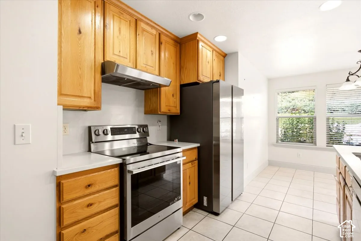 Kitchen featuring wood cabinetry, stainless steel appliances, solid surface countertops, recessed lighting, and tile flooring