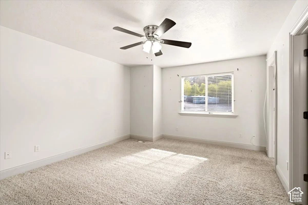 Bedroom featuring neutral-toned carpeting, a multi-blade ceiling fan with integrated lighting, and a window with horizontal blinds