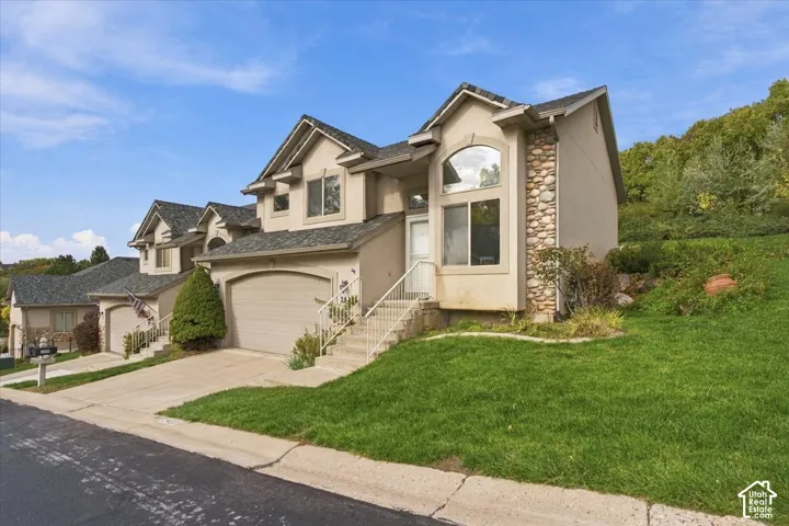 Exterior featuring stucco siding, stone veneer accents, multi-gabled roofline, concrete driveway, and covered entryway