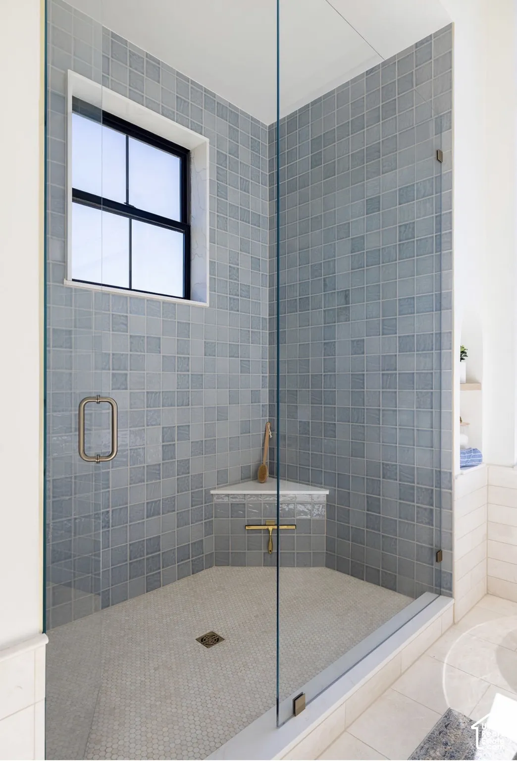 Walk-in shower featuring blue square tile surround, frameless glass enclosure, built-in corner bench with stone top, and grid-pattern window with black frame