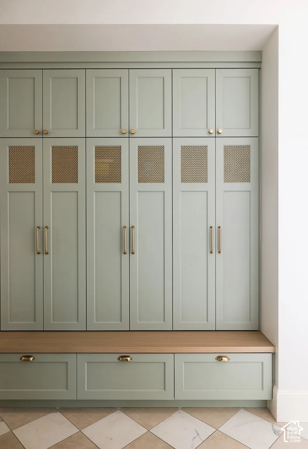 Built-in floor-to-ceiling cabinetry with sage green shaker-style doors, integrated rattan upper door panels, wood-finish bench seating, brass-tone hardware, and diamond-patterned stone flooring