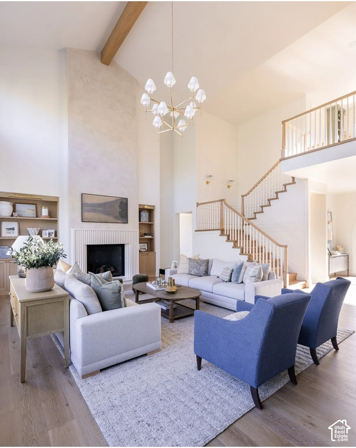 Double-height ceiling featuring a exposed wooden structural beam, floor-to-ceiling fireplace with reeded detailing, built-in cabinetry, wood-finish flooring, and a staircase with a wooden handrail