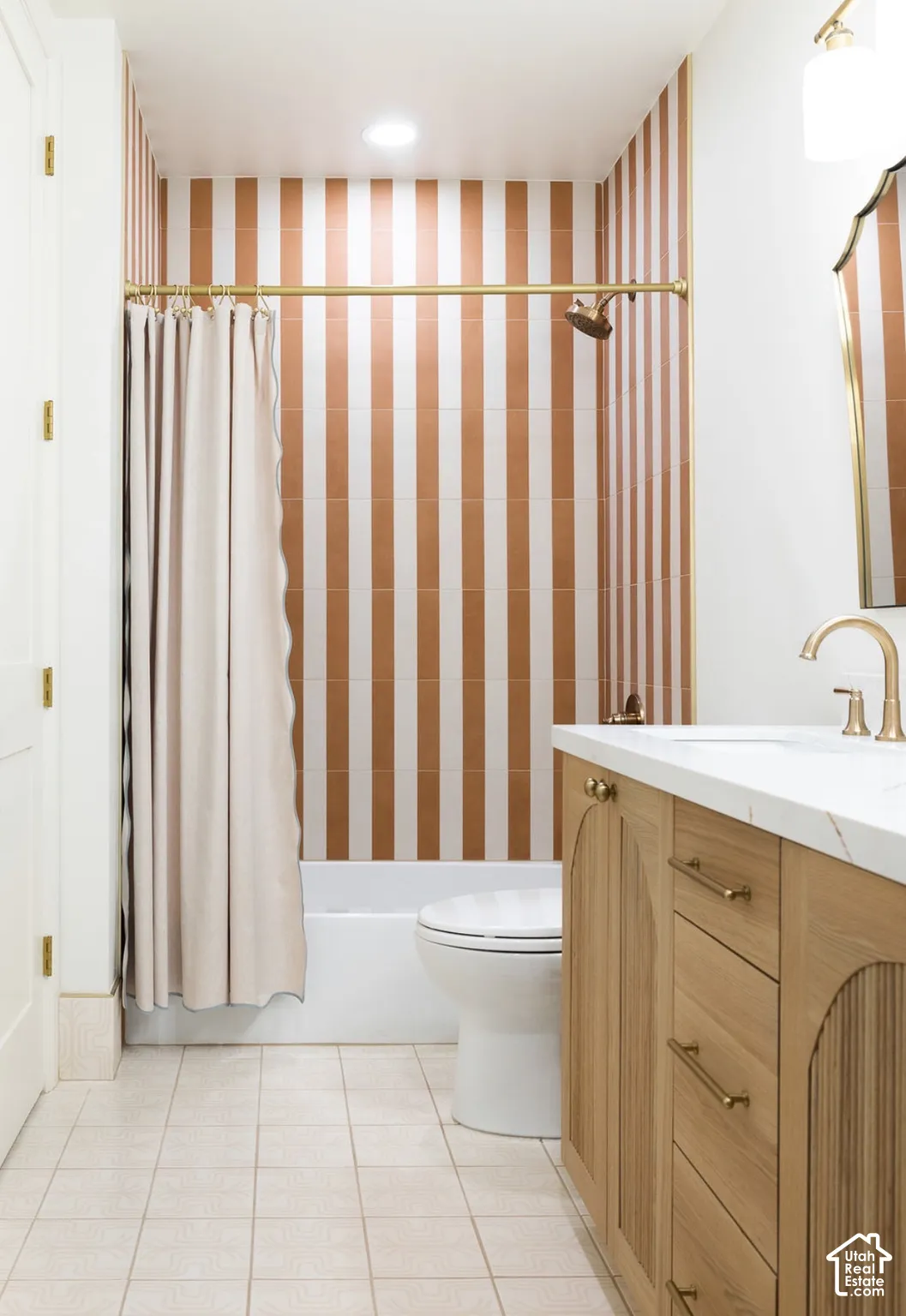 Bathroom featuring a custom wood vanity with arched cabinet detailing, white stone countertop, brass-finish fixtures, and vertical striped wall tile