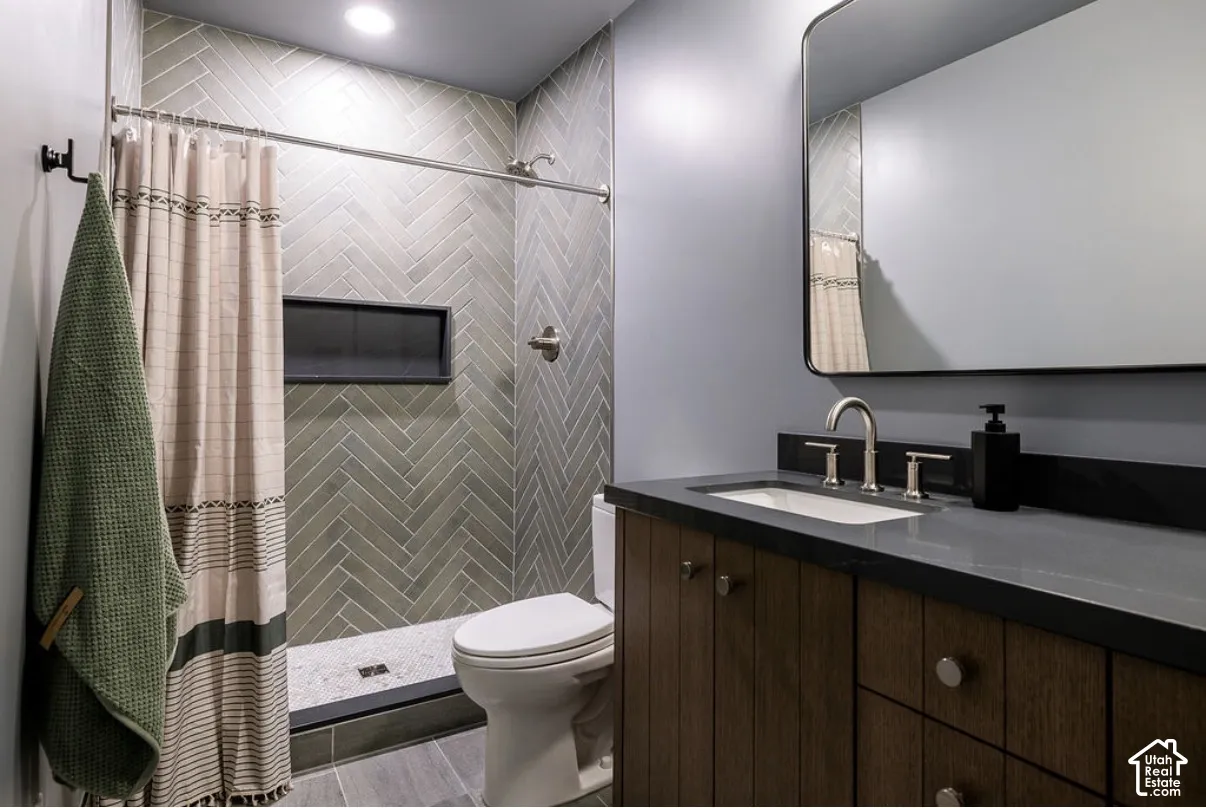 Bathroom featuring a herringbone-pattern tile shower surround with integrated wall niche, dark wood-finish cabinetry, stone-composite countertop, and a rectangular undermount sink with a metallic finish faucet