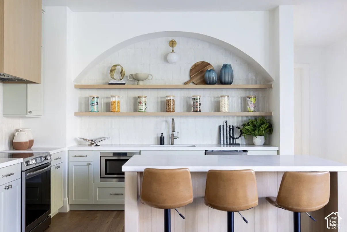 Kitchen featuring an arched recessed wall with vertical tile backsplash and tiered wood shelving, quartz countertops, a built-in microwave, and an island with wood-finish paneling