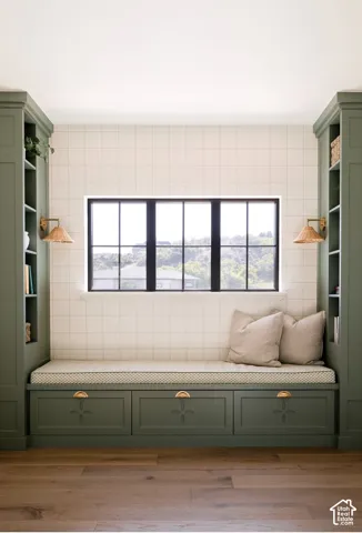 Built-in cabinetry featuring sage green millwork, integrated shelving, pull-out storage drawers with brass hardware, grid-pattern tiled wall, and wood-finish flooring