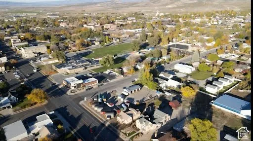 Aerial perspective of the surrounding community featuring paved roadway infrastructure, mixed-density development, established deciduous trees, and surrounding mountainous terrain