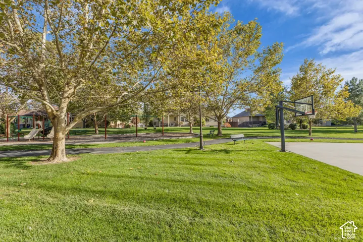 Recreational area featuring a concrete basketball court, playground equipment, mature shade trees, paved walkways, and designated seating