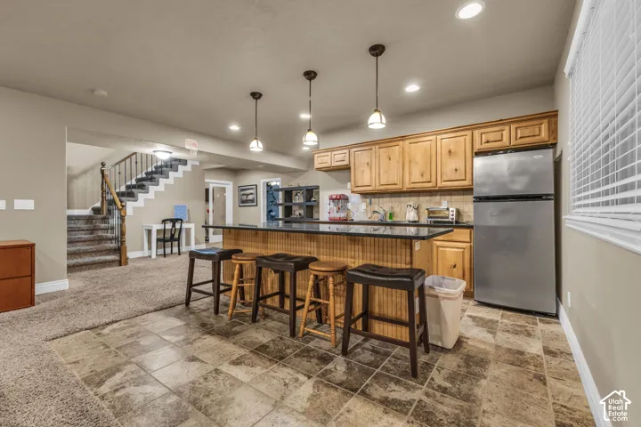 Kitchenette featuring a stone-topped island with beadboard detailing, natural wood cabinetry, pendant lighting, stainless steel refrigerator, and tiled flooring