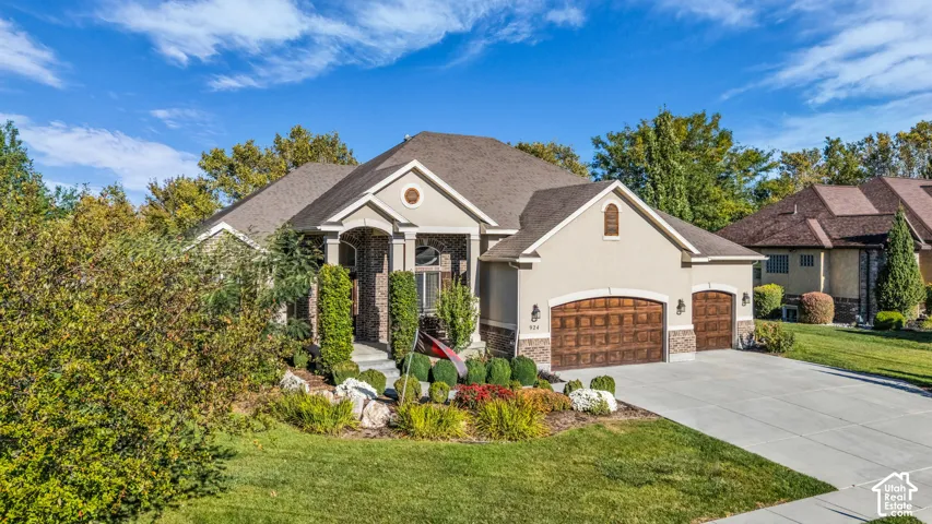 Stucco and brick facade with a covered entryway, decorative stone accents, and a three-car garage featuring segmented carriage-style doors