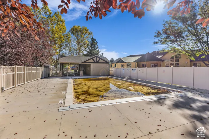 Outdoor swimming pool featuring a concrete surround, privacy fencing, and an attached covered pavilion