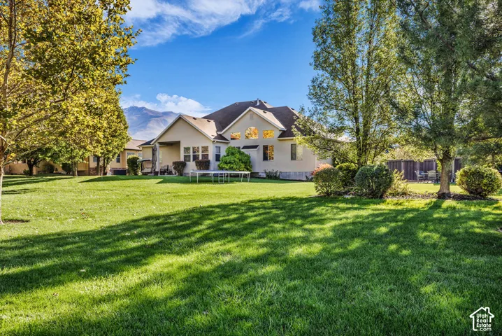 Expansive backyard featuring a manicured lawn, mature trees, and a mountain backdrop