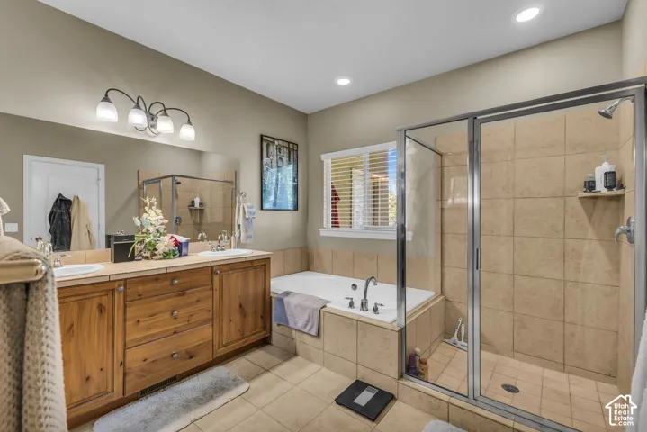 Bathroom featuring a dual-sink wooden vanity, a large framed mirror, a built-in soaking tub, and a glass-enclosed shower with tiled walls and flooring