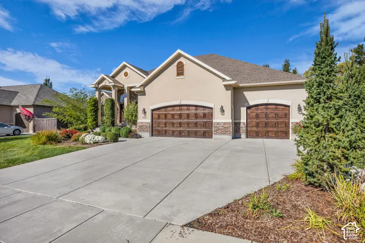 Stucco exterior with stone-accented garage base, multi-car garage with arched, wood-finish doors, and concrete driveway