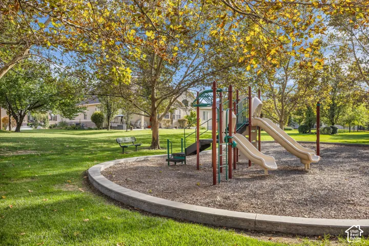 Expansive grounds featuring a playground structure with dual slides, mature shade trees, a curved concrete border, and a metal bench