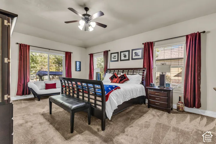 Spacious room featuring neutral wall tones, wall-to-wall carpeting, multiple windows with dark curtain rods, and a central ceiling fan with multi-light fixture