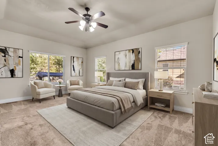Neutral-toned bedroom featuring a tray ceiling, plush carpeting, multiple windows, and a ceiling fan with integrated lighting
