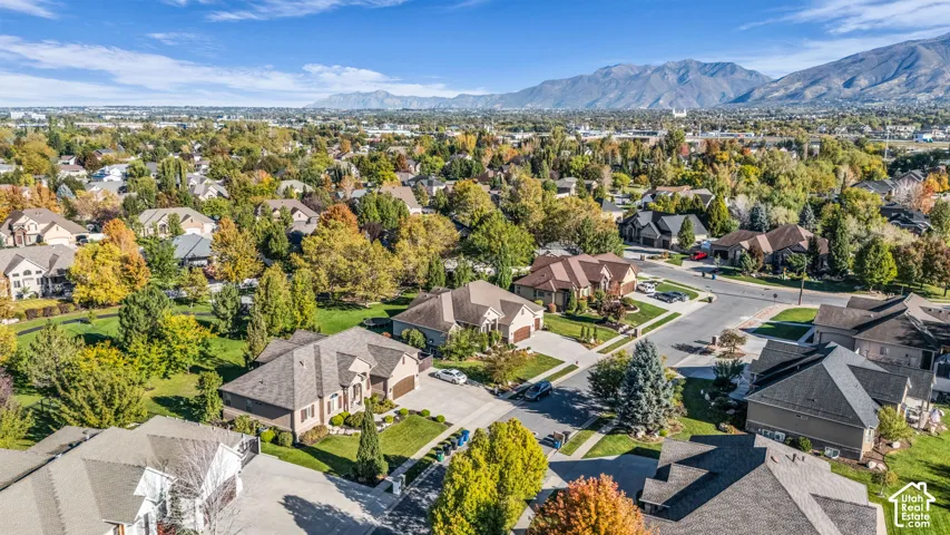 Aerial perspective featuring detached single-family residences, concrete driveways, expansive lawn areas, mature deciduous trees, and a mountain backdrop