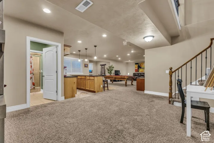 Open-concept interior featuring a built-in wet bar with cabinetry and stone-finish countertops, recessed lighting, carpeted flooring, and a staircase with a wooden handrail and metal balusters
