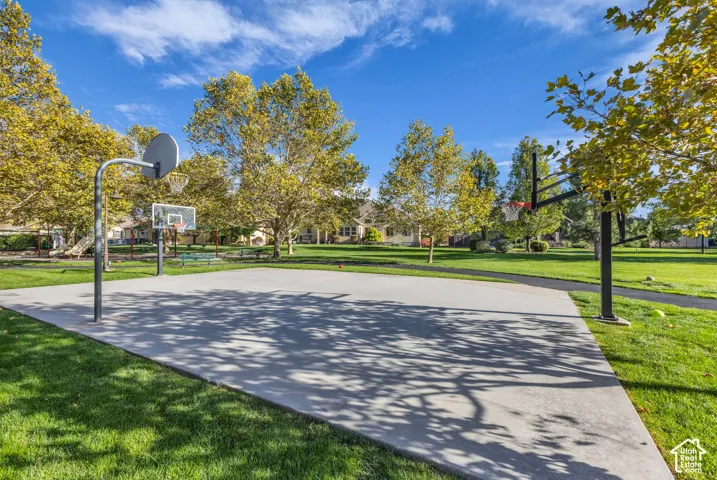 Outdoor recreational area featuring a concrete basketball court, two steel-framed hoop systems, and expansive green space with mature deciduous trees