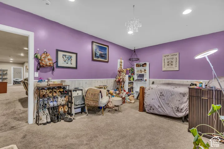 Interior space featuring neutral-tone carpeting, recessed ceiling lighting, a decorative chandelier, and wainscoting