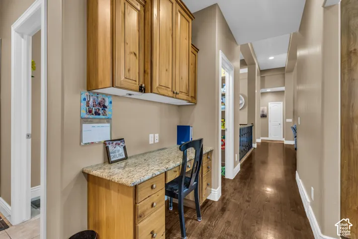 Built-in workspace featuring light wood cabinetry, stone-surface countertop, and wood-finish flooring