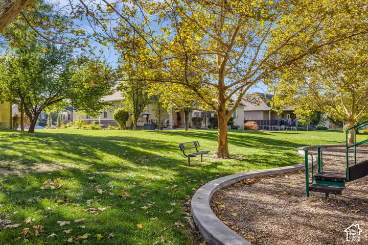 Expansive grounds featuring a manicured lawn, mature trees, concrete curbing, and a multi-level playground structure