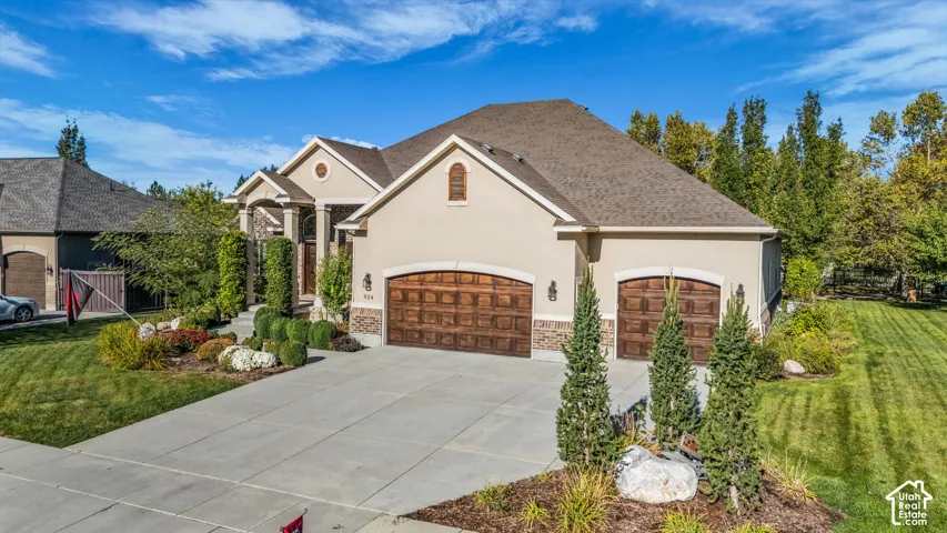 Stucco exterior featuring stone accents, a three-car garage with arched wooden-finish doors, and a concrete driveway