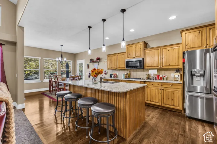 Kitchen featuring natural wood cabinetry, stone-surface countertops, central island with seating, stainless steel appliances, and wood-finish flooring