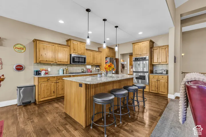 Kitchen featuring wood cabinetry, stone countertops, stainless steel double wall ovens, a center island with beadboard detailing, and recessed and pendant lighting