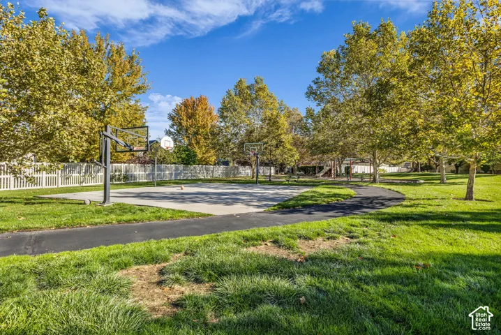 Concrete basketball court with integrated hoops, paved pathway, perimeter privacy fencing, and mature trees on expansive grounds