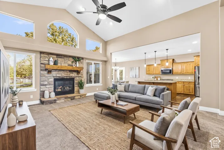 Vaulted ceilings featuring a central overhead fan, stone-surround fireplace with a timber mantel, and expansive arched windows
