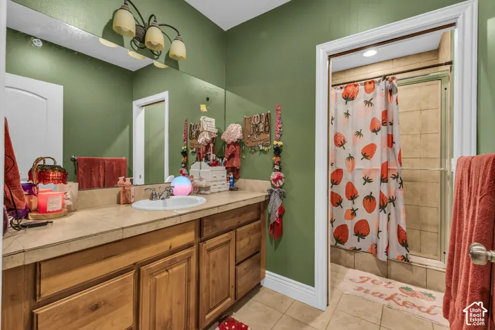 Bathroom featuring a wooden vanity with tile countertop, integrated basin sink, large wall-mounted vanity mirror, multi-bulb light fixture, and walk-in shower with tile surround