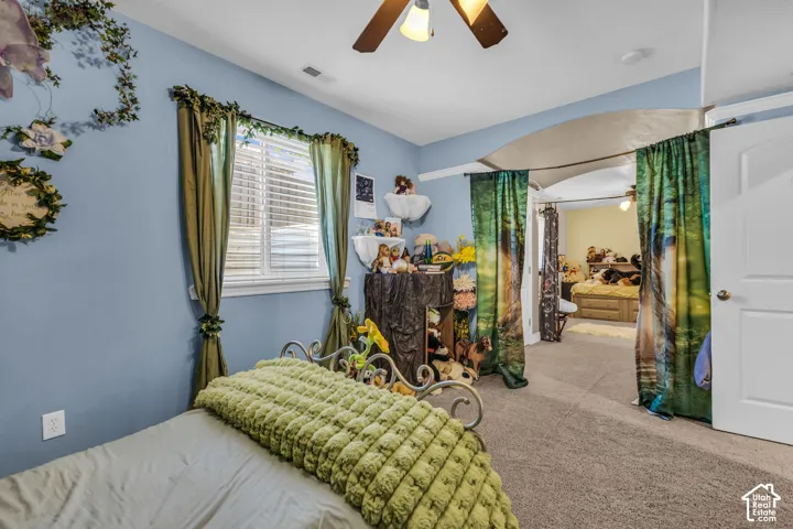 Bedroom featuring neutral carpeting, an arched architectural opening, a ceiling fan with light fixture, and a dual-pane window