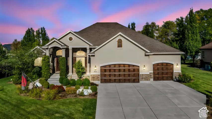 Stucco and brick facade with a hipped roof, arched entryway, and attached three-car garage featuring segmented wooden doors