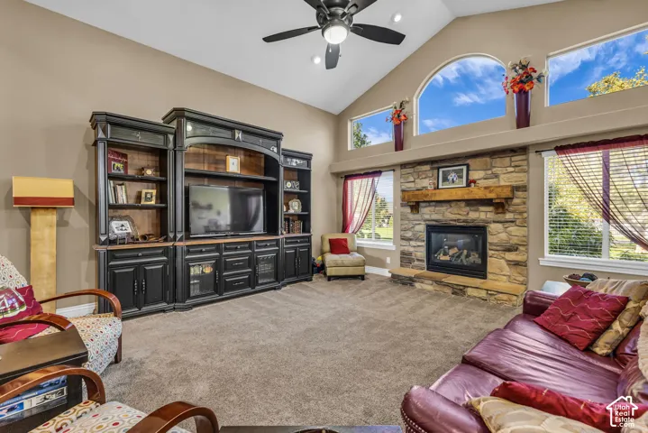 Vaulted ceilings with a ceiling fan, stone-surround fireplace with a timber mantel, and built-in dark cabinetry featuring glass-front display sections and arched transom windows