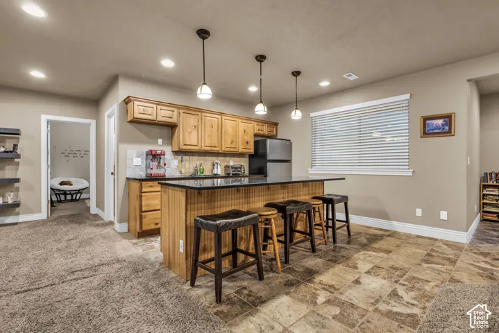 Kitchen featuring wooden cabinetry, dark stone-finish countertops, tile flooring, and three glass pendant lights suspended over an island